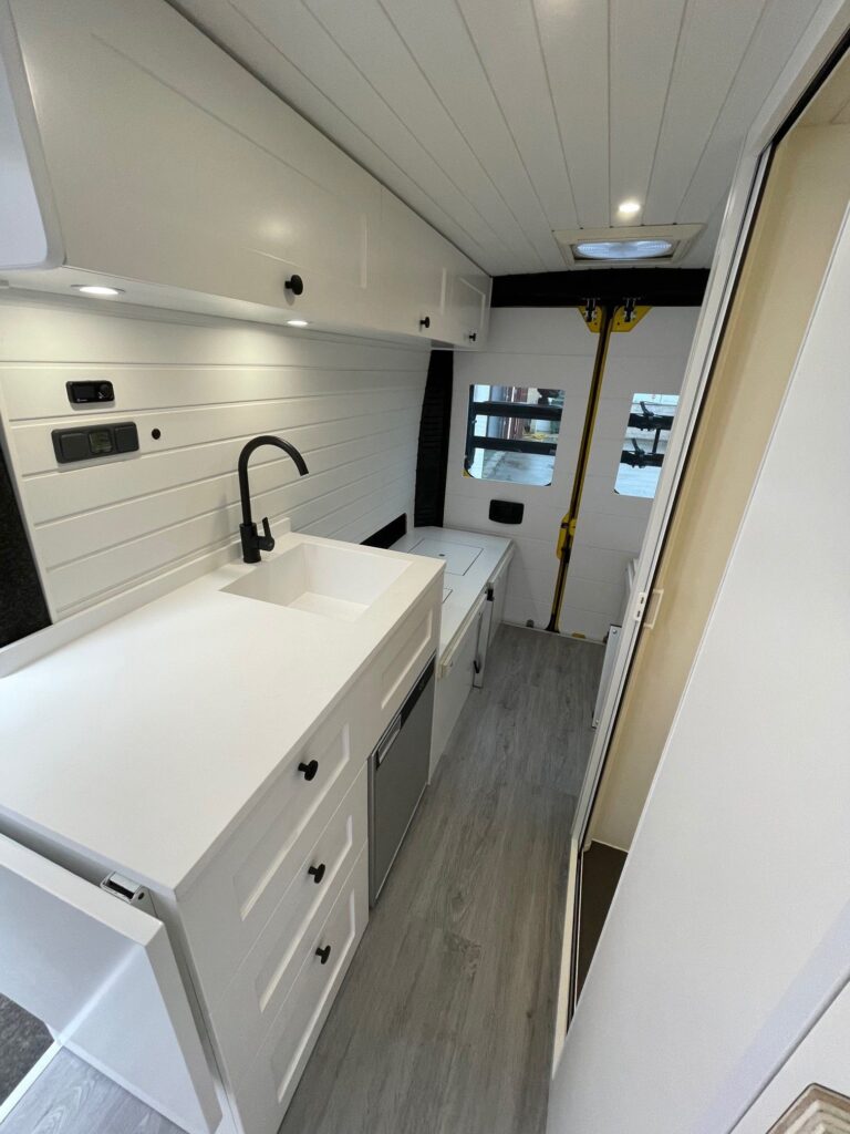 Detalle de la cocina con fregadero, cajones y estantes suspendidos para almacenamiento en la Peugeot Boxer L3H2 4+2 CORIAN, Camperización por Baovan Camper.