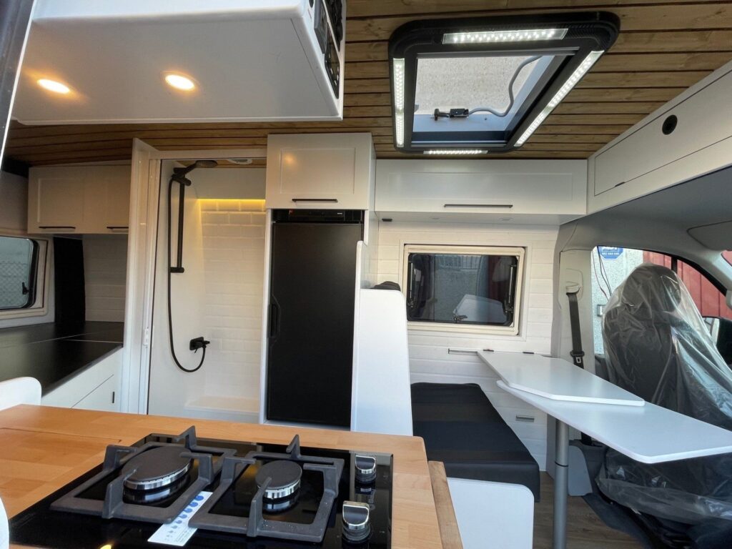 VW Crafter L2H2 2+2 con interior iluminado, mesa plegable, asientos, baño y cocina.