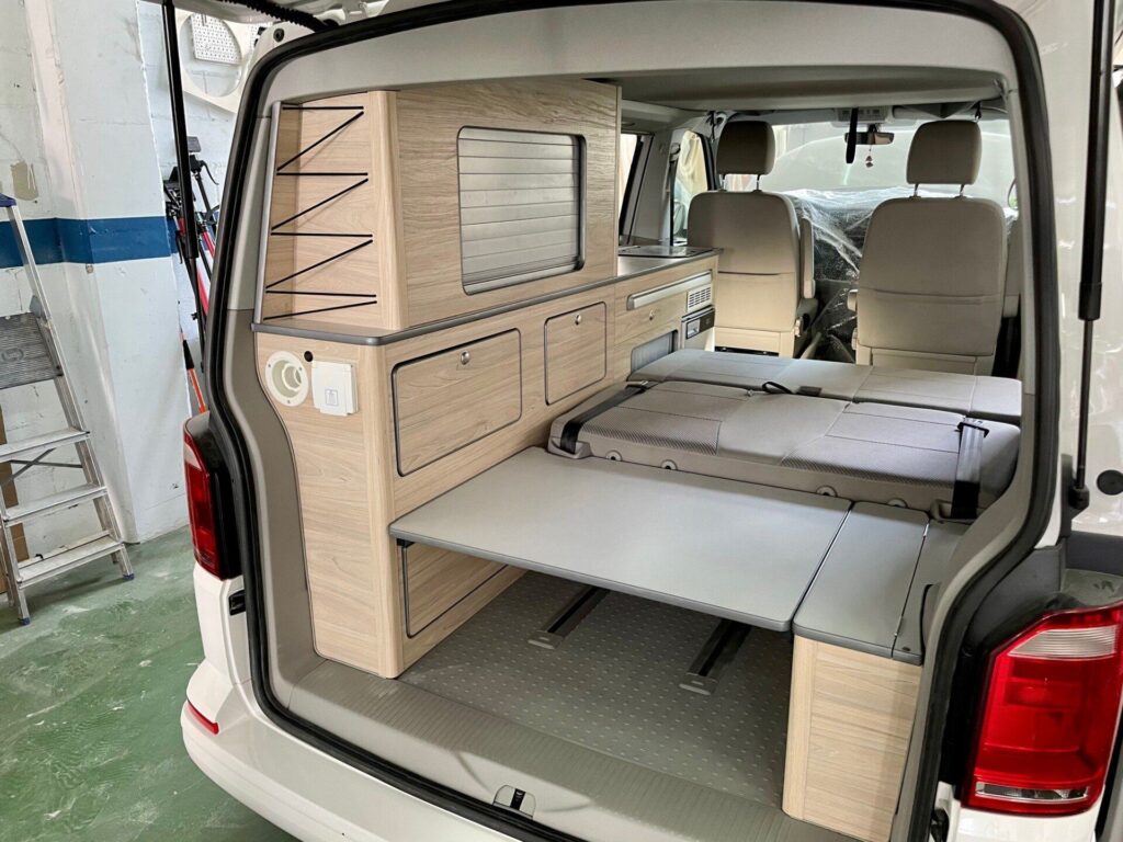Interior de la Camper California T6 con mueble lateral que incluye estantes para almacenamiento