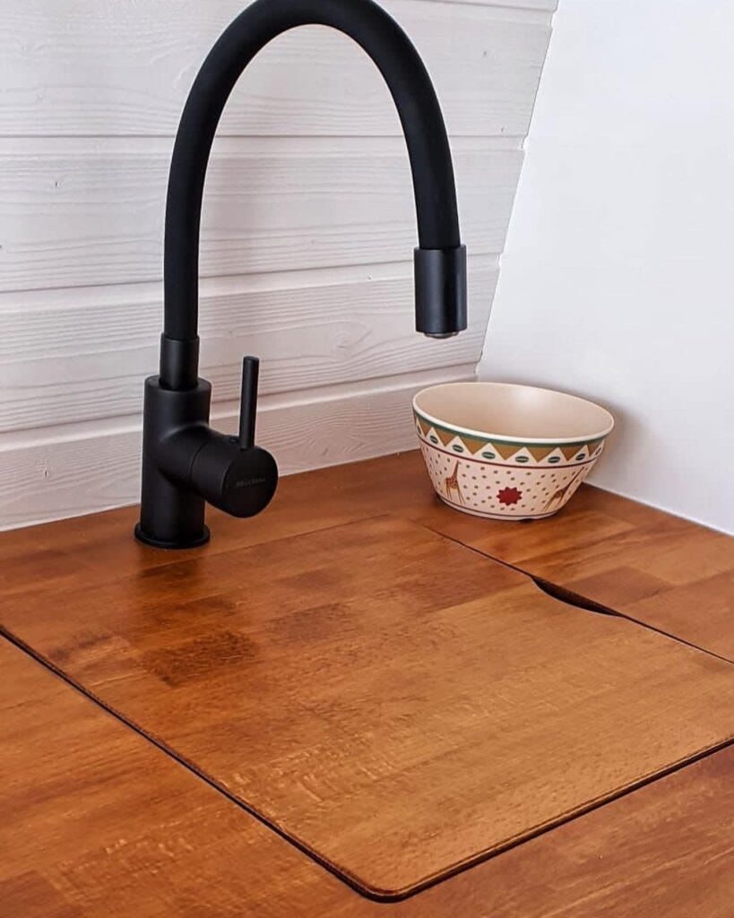 Imagen de una encimera de madera en la furgoneta camperizada Boxer L3H2 2+2, con un grifo de cuello alto de color negro y un cuenco decorativo a la derecha.
