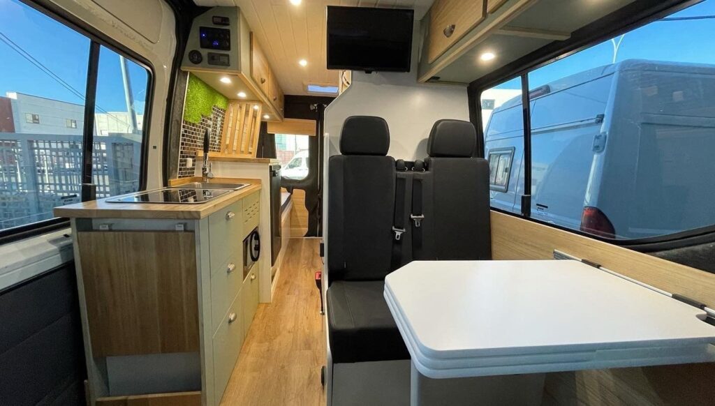 Vista de la Iveco Daily 4+4 Pawlonia desde el asiento del conductor, con mesa plegable, cocina y camas al fondo. Camperizado por BaovanCamper