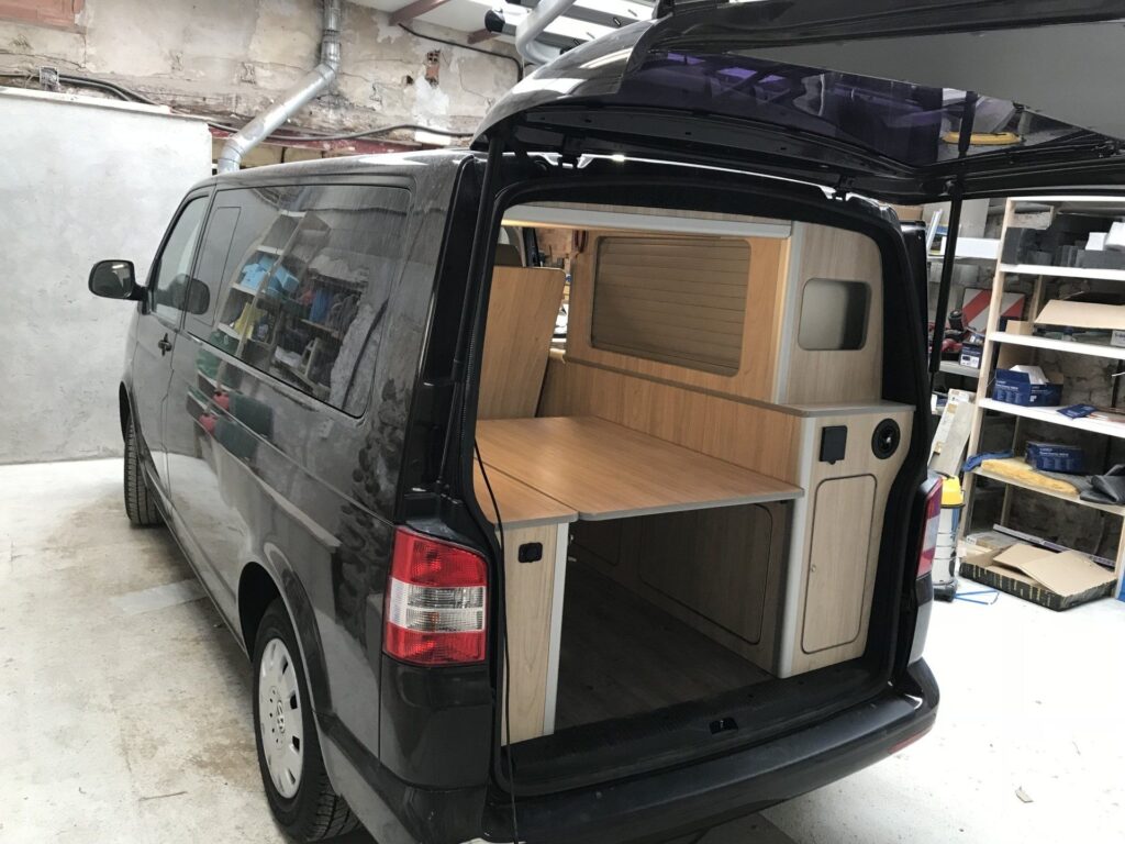 Puerta trasera abierta mostrando la estructura de la cama y armarios en la Camper Volkswagen Transporter T5 convertida por Baovan.