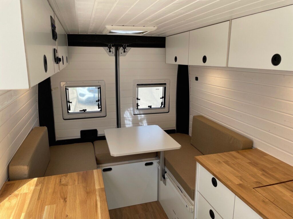 Área de estar de la Fiat Ducato L2H2, convertida por Baovan Camper, con mesa retráctil y sofás cómodos para dos.