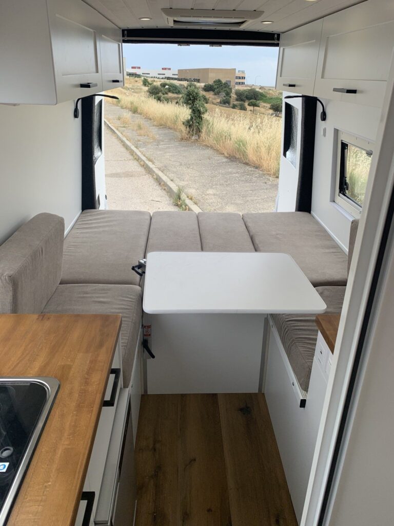 Detalle de la zona de descanso con sofás y mesa extensible, muy confortable, en la Camper Mercedes Sprinter L3H2 4+4. Camperizado por BaovanCamper.