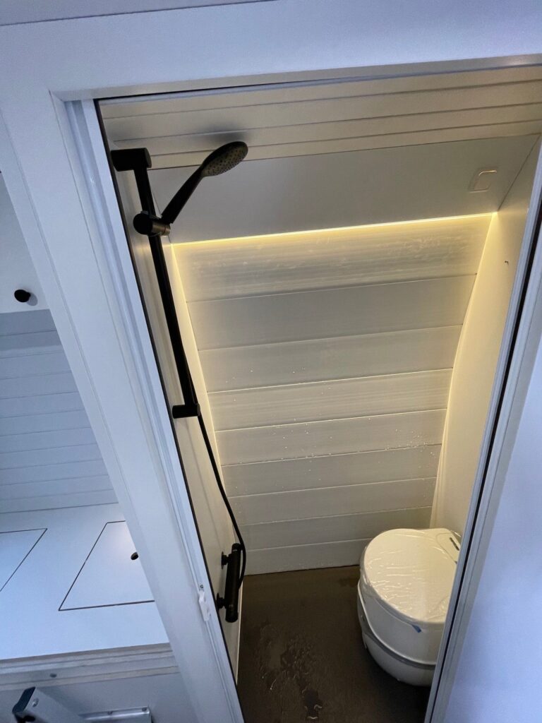 Detalle del baño completo con inodoro y ducha suspendida, iluminación elegante en la Peugeot Boxer L3H2 4+2 CORIAN, Camperización por Baovan Camper.