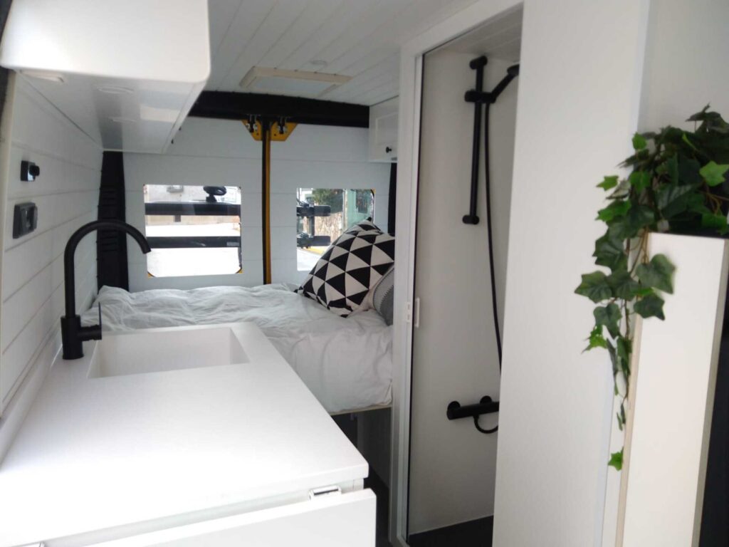 Vista interna de la Peugeot Boxer L3H2 4+2 CORIAN, Camperización por Baovan Camper, con cama al fondo, fregadero, baño, todo en blanco y elegante.