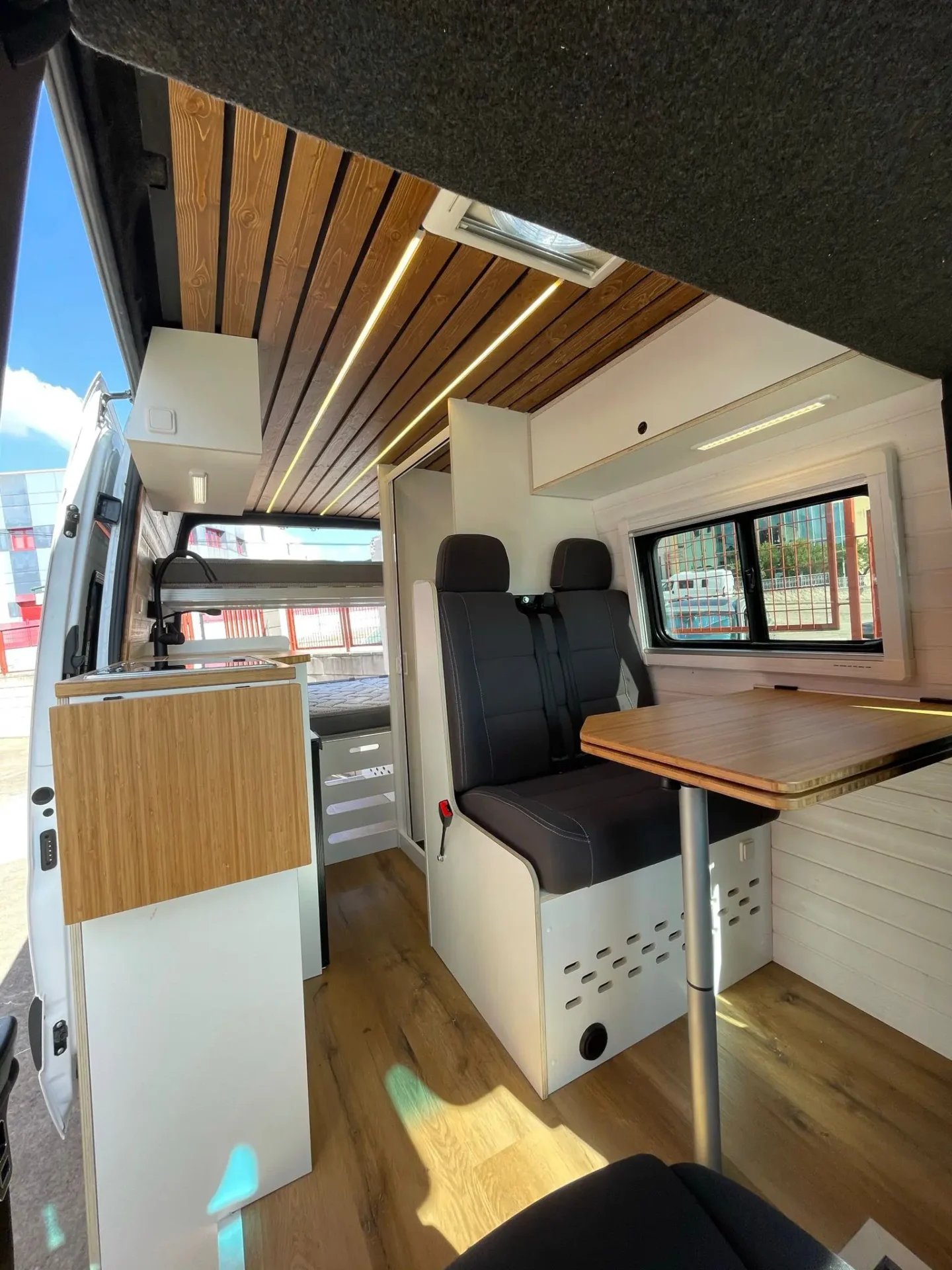 MB Sprinter Camper 4+4 Con Estilo con vista hacia atrás, mesa, techo moderno y acabados claros.