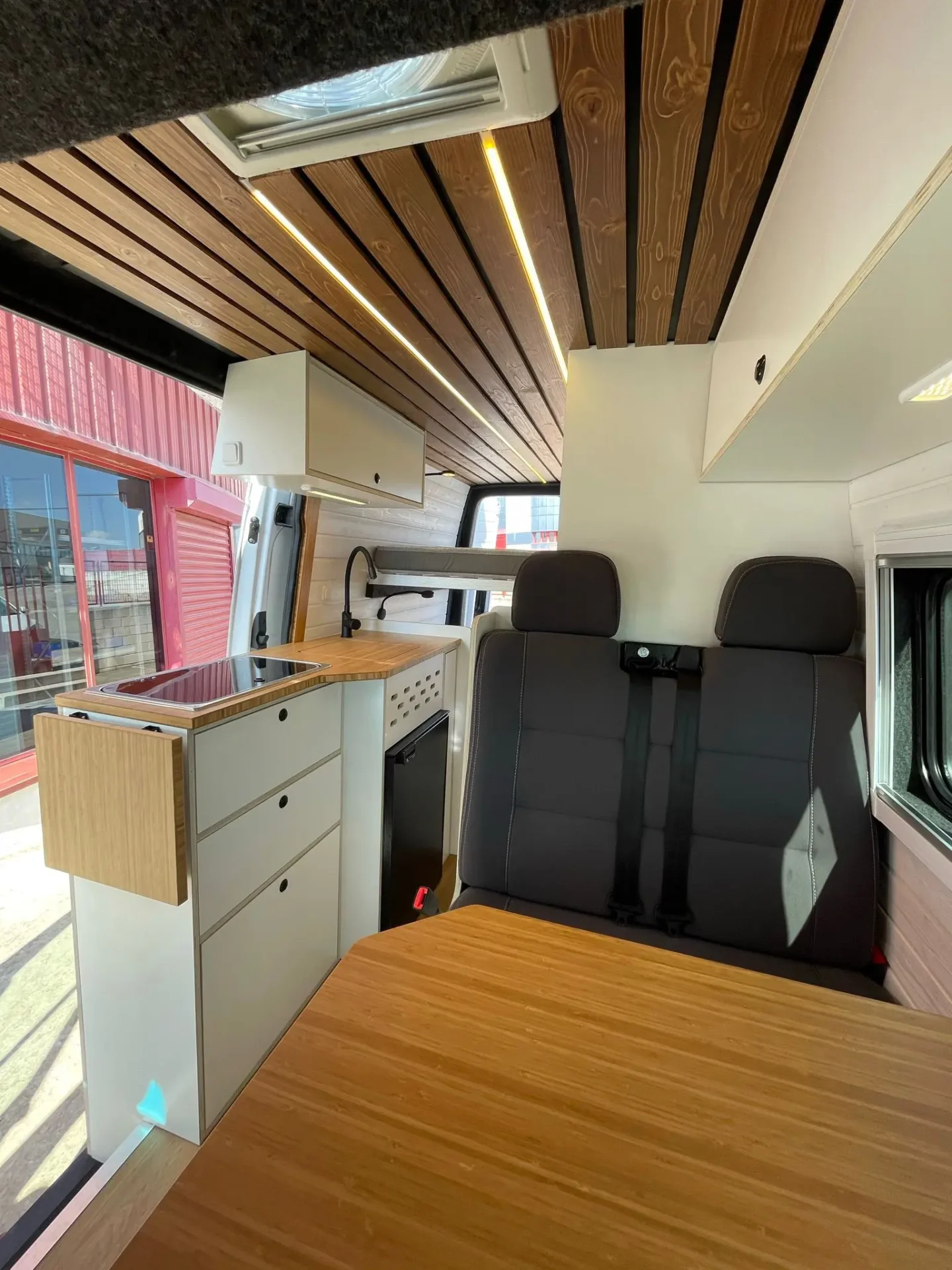 MB Sprinter Camper 4+4 Con Estilo con vista hacia atrás, mesa, techo moderno y acabados claros.