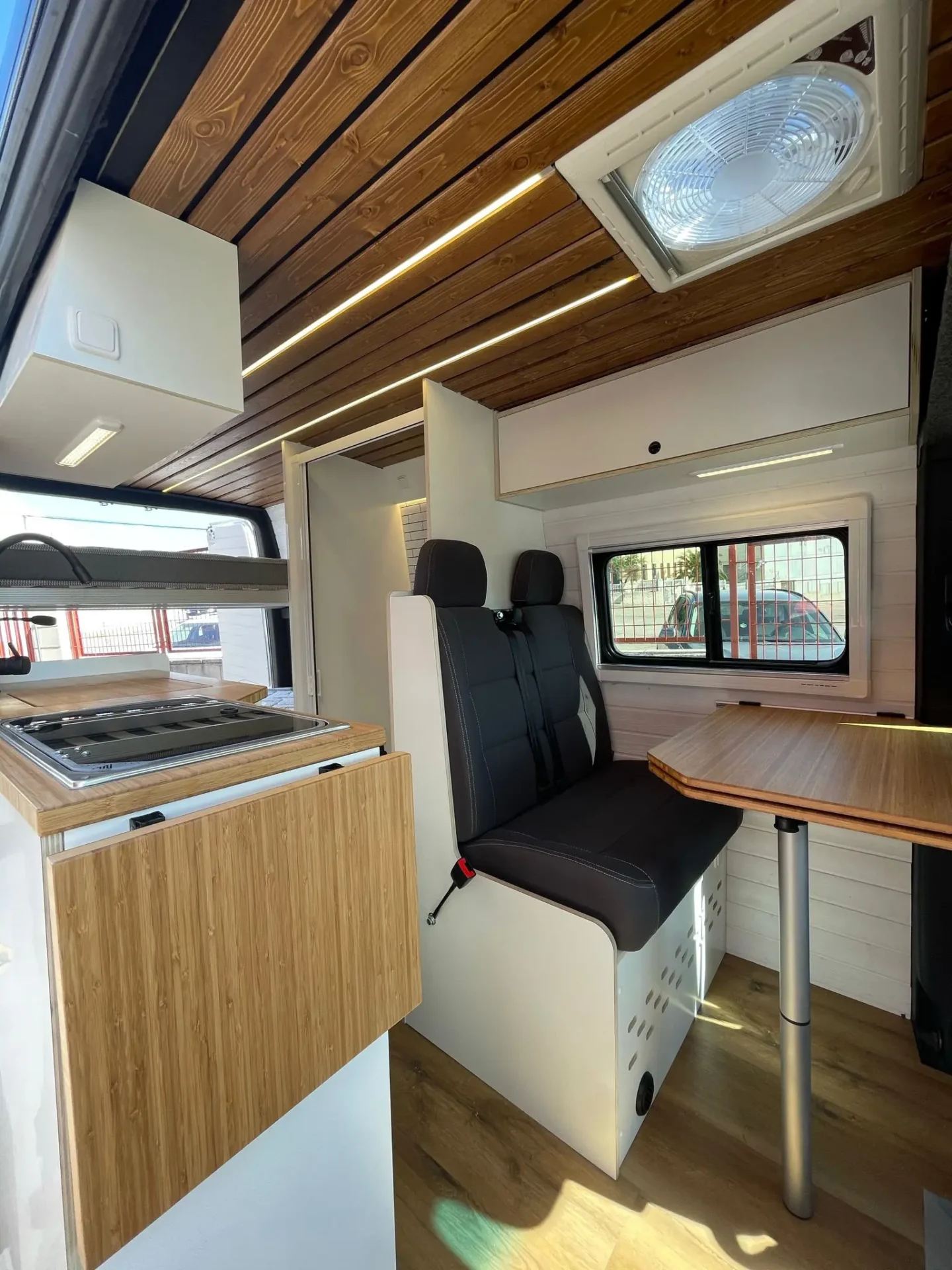 MB Sprinter Camper 4+4 Con Estilo con vista hacia atrás, mesa, techo moderno y acabados claros.