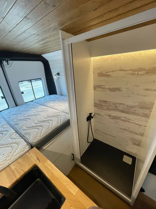 Interior de una camper L3H2 mostrando la zona de entrada con escalón iluminado, paredes de revestimiento claro y piso de madera laminada.