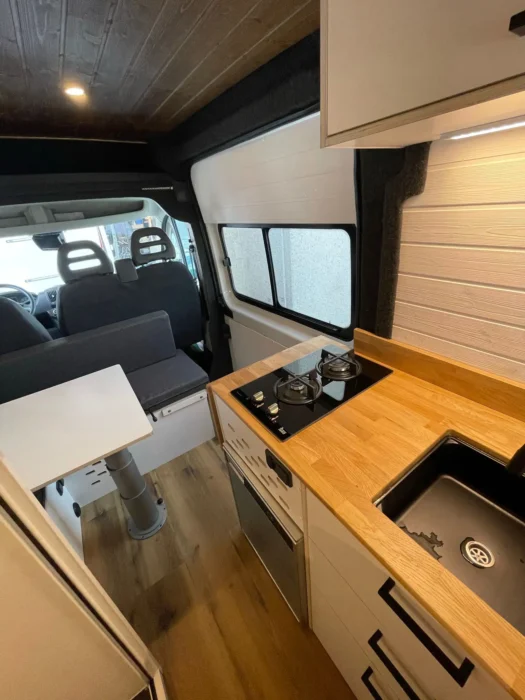 Vista desde la cabina hacia la parte trasera de la camper L3H2, con mesa de comedor, cocina a la derecha y asientos en 'L' al fondo.
