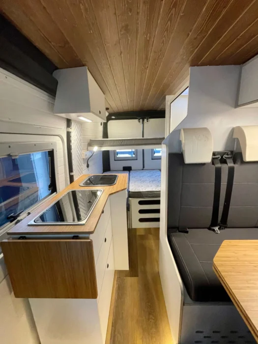 Interior de la Peugeot Boxer Camper mirando hacia la cabina, destacando la zona de comedor con asientos ergonómicos y acabados en madera.