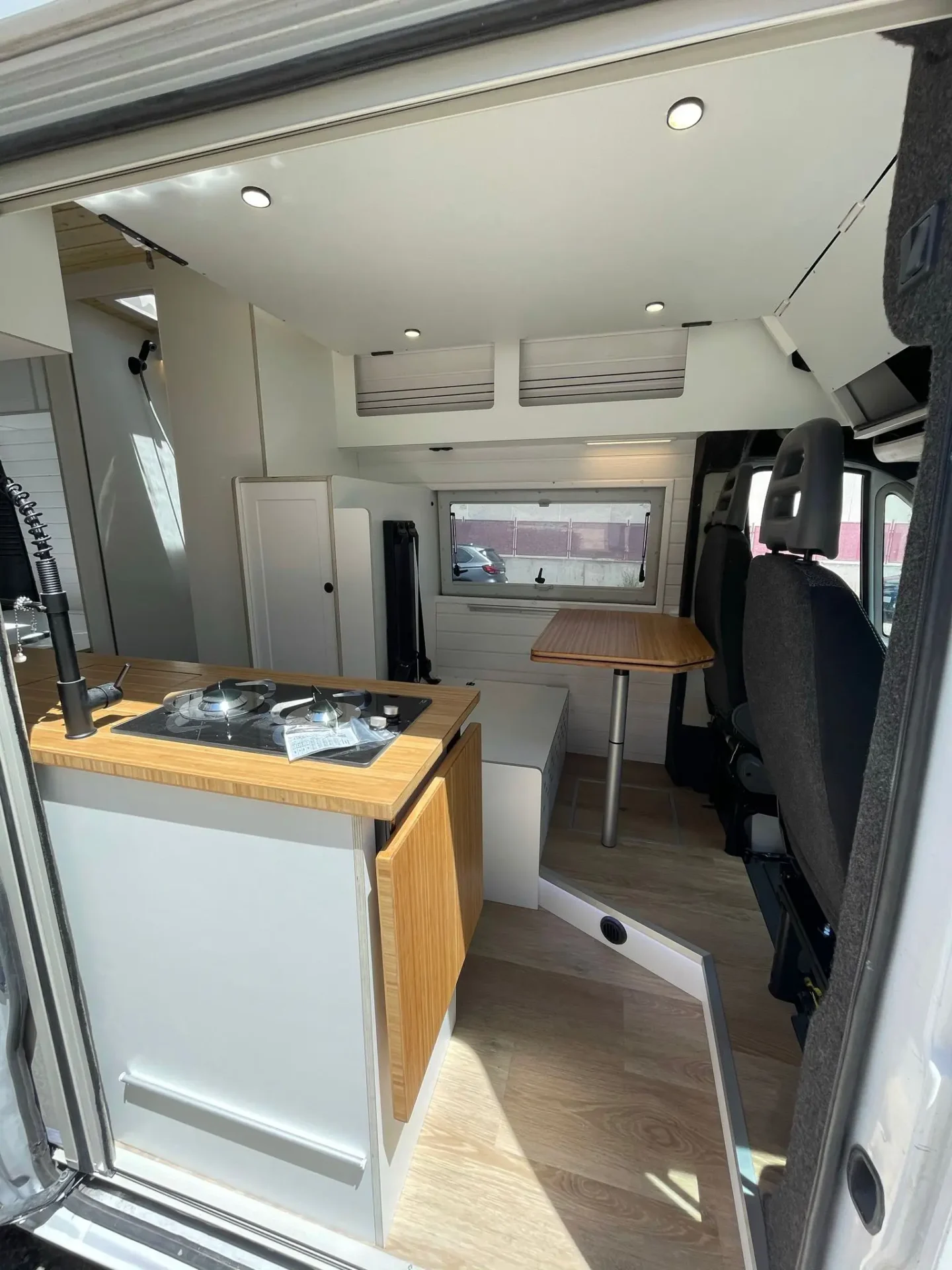 Vista interior de la Ducato L4H3 camperizada hacia la zona de conducción, cama abatible, techo con acabado de madera y amplio espacio de almacenamiento.