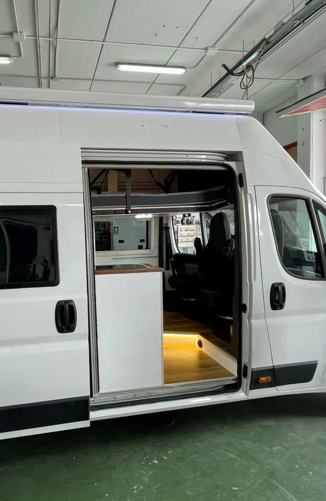 Vista lateral de la Fiat Ducato L3H3 con puerta abierta, mostrando el interior y la cama abatible.