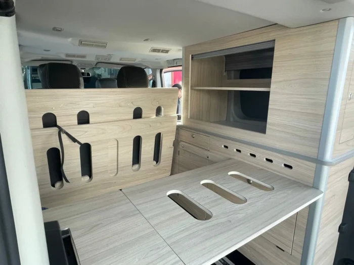Detalles de la cama plegable en madera clara en la Renault Trafic Camper.