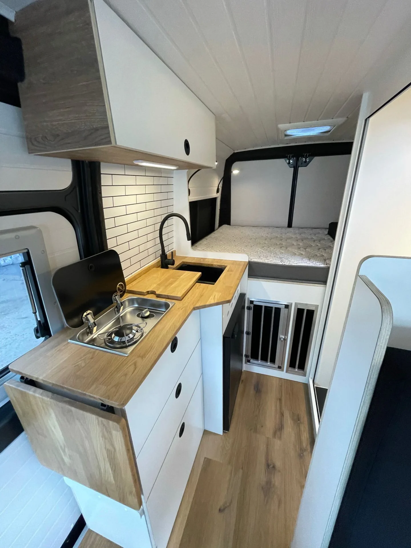 Cocina equipada con armarios blancos, amplio espacio de almacenamiento, zona de preparación de alimentos, fregadero, baño y cama con claraboya
