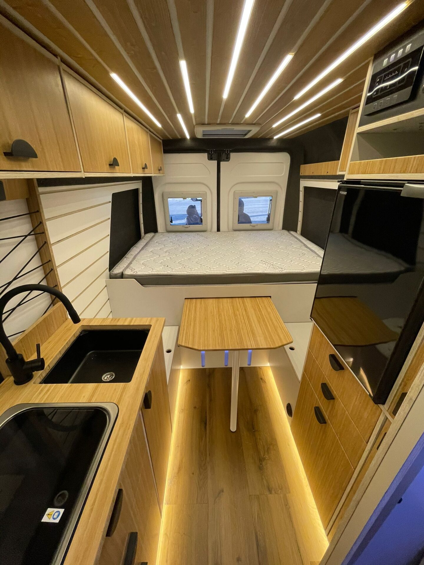 Furgoneta camperizada con mesa plegable abierta. La mesa se guarda debajo de la cama.
