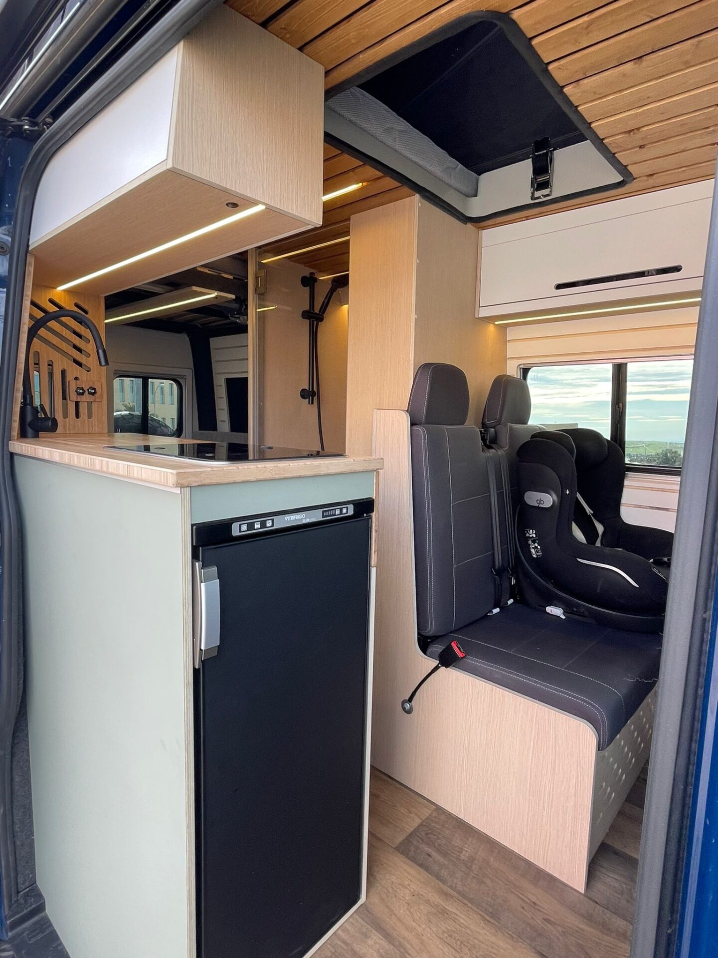 Interior de camper Baovan mostrando la nevera empotrada y los asientos delanteros giratorios con acceso a la cabina.