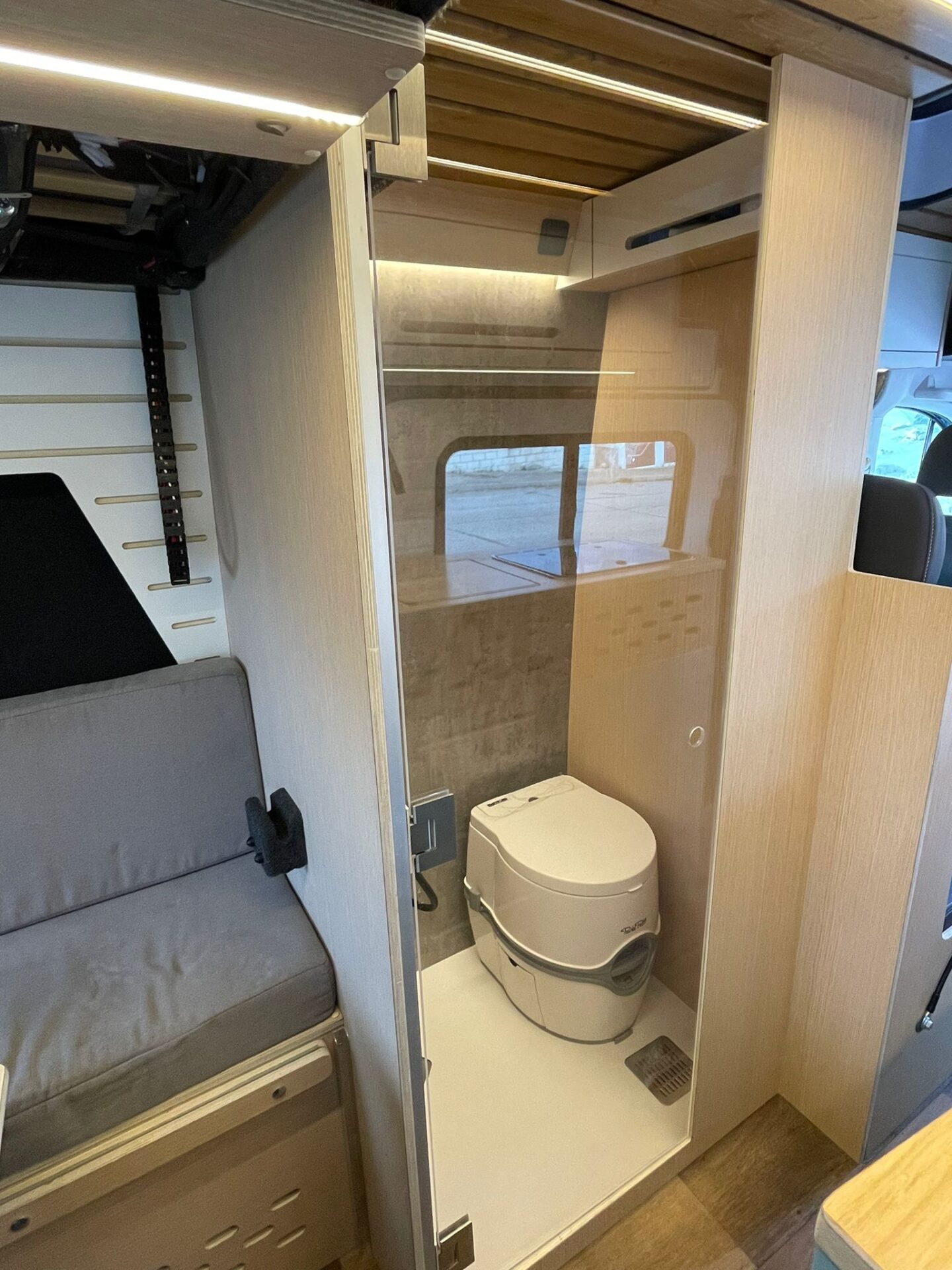 Baño compacto en camper Baovan con WC portátil y ducha con puertas de persiana corredera, optimizando el espacio y la funcionalidad.