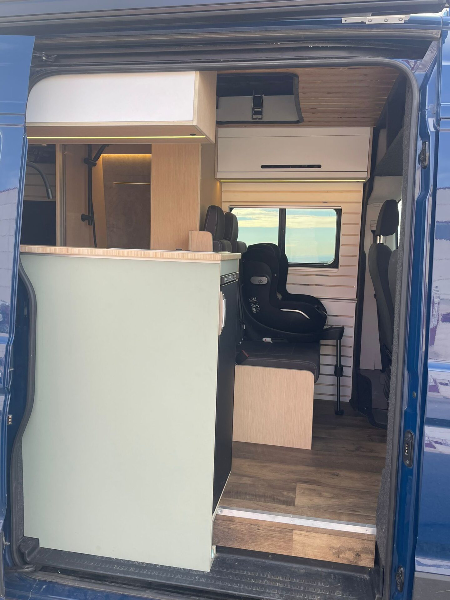 Vista desde la puerta lateral del camper Baovan con techo elevable, mostrando los asientos delanteros giratorios y la elegante distribución interior.