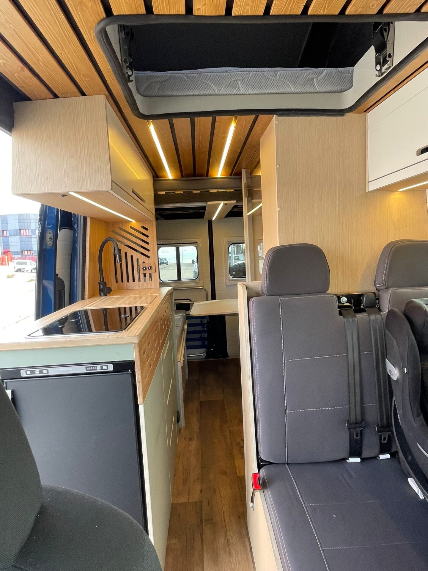 Espacioso interior de camper Baovan con vista hacia los asientos delanteros giratorios, cocina completa y almacenamiento superior.