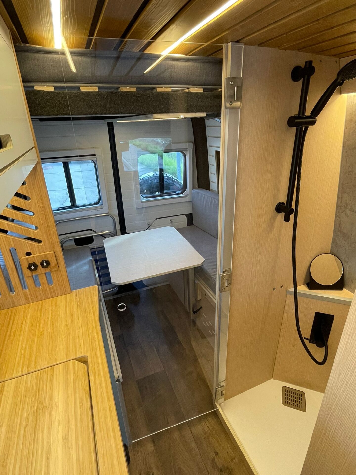 Interior de una camper Baovan detallando la zona de ducha convertible y área de comedor con iluminación ambiental.