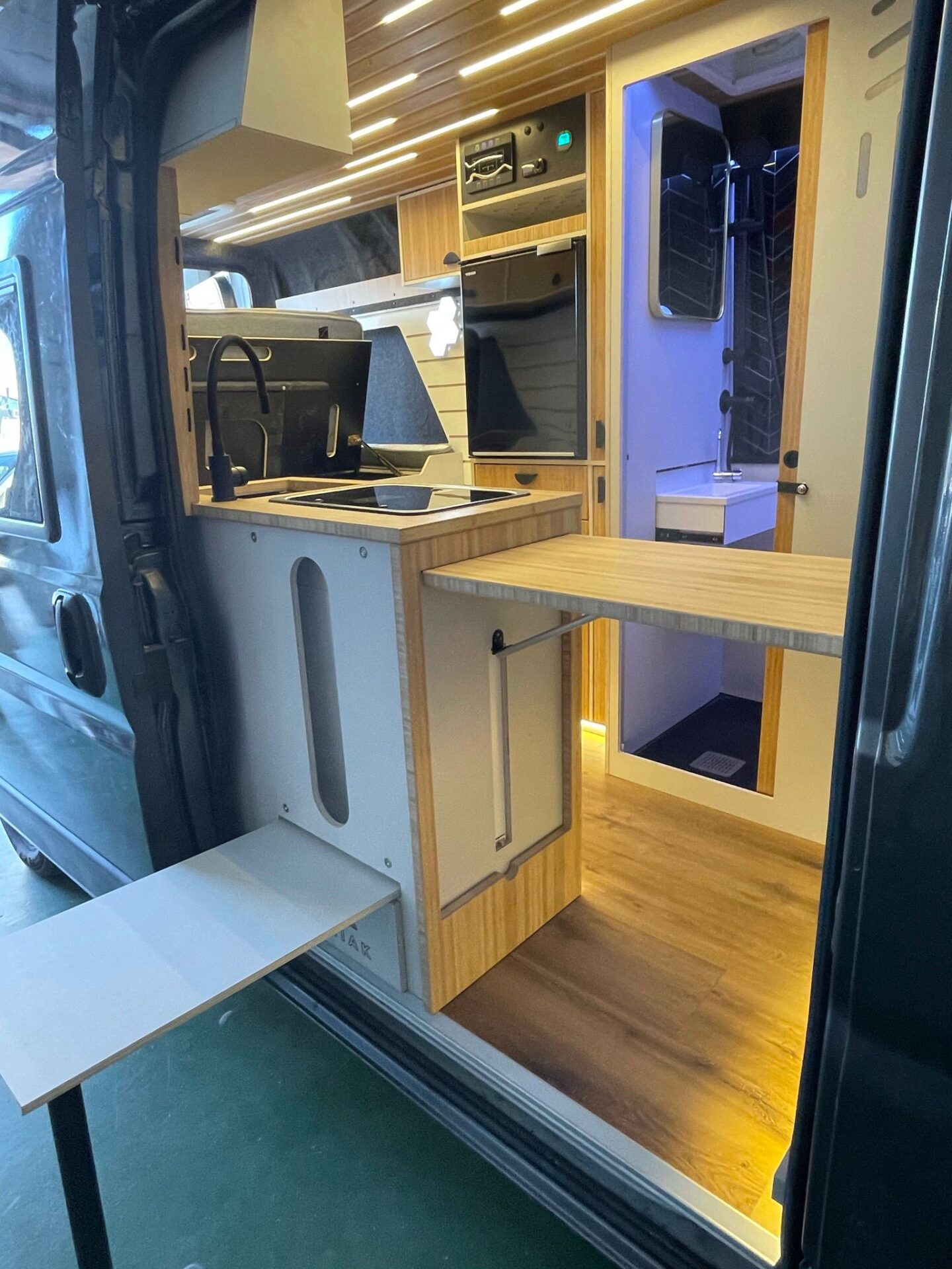 Vista del interior de camper Baovan con mesa plegable, cocina de gas integrada y estantes de almacenamiento.