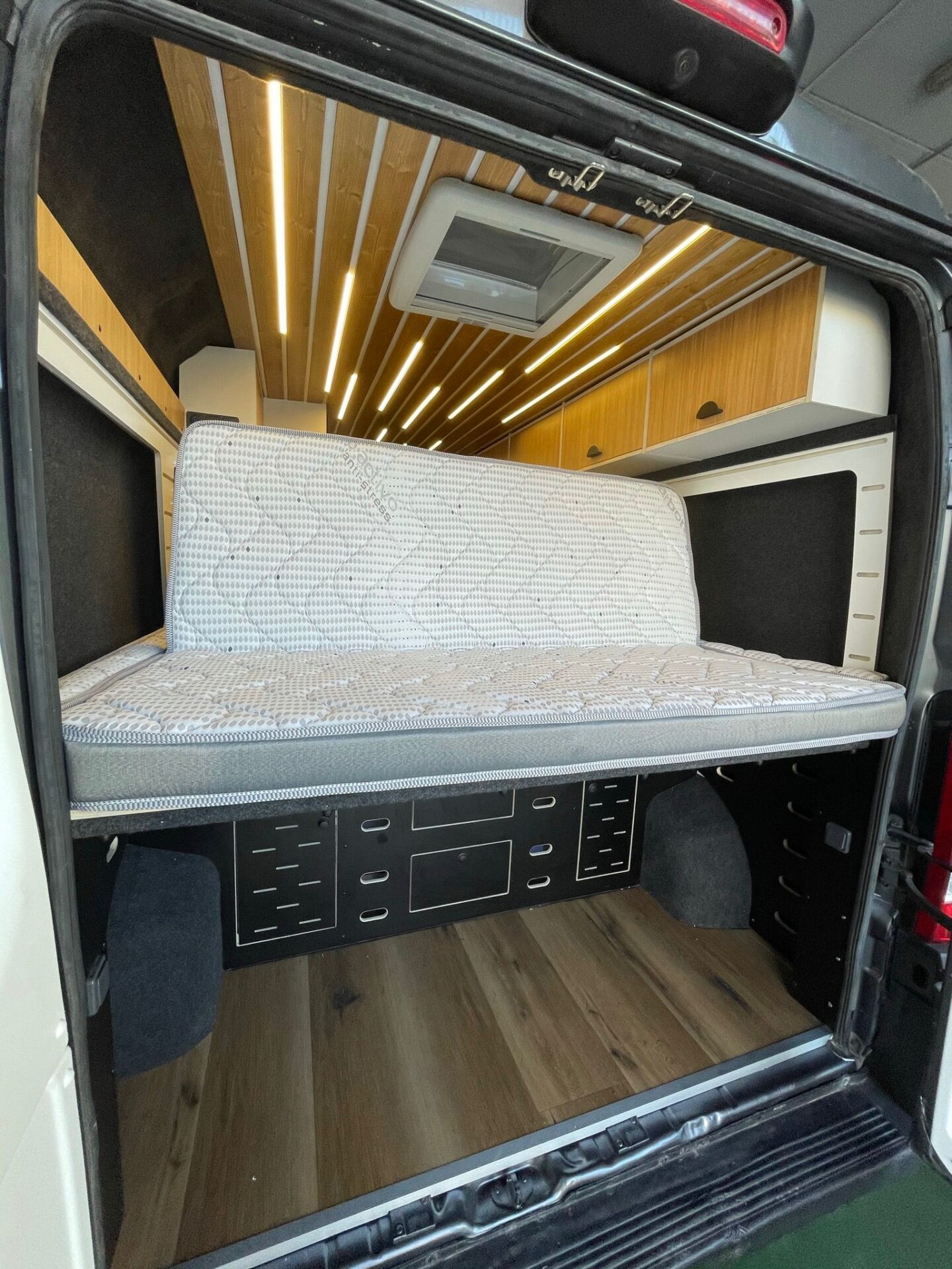 Cama amplia en el área trasera del camper Baovan, con iluminación ambiental y espacio de almacenamiento debajo.